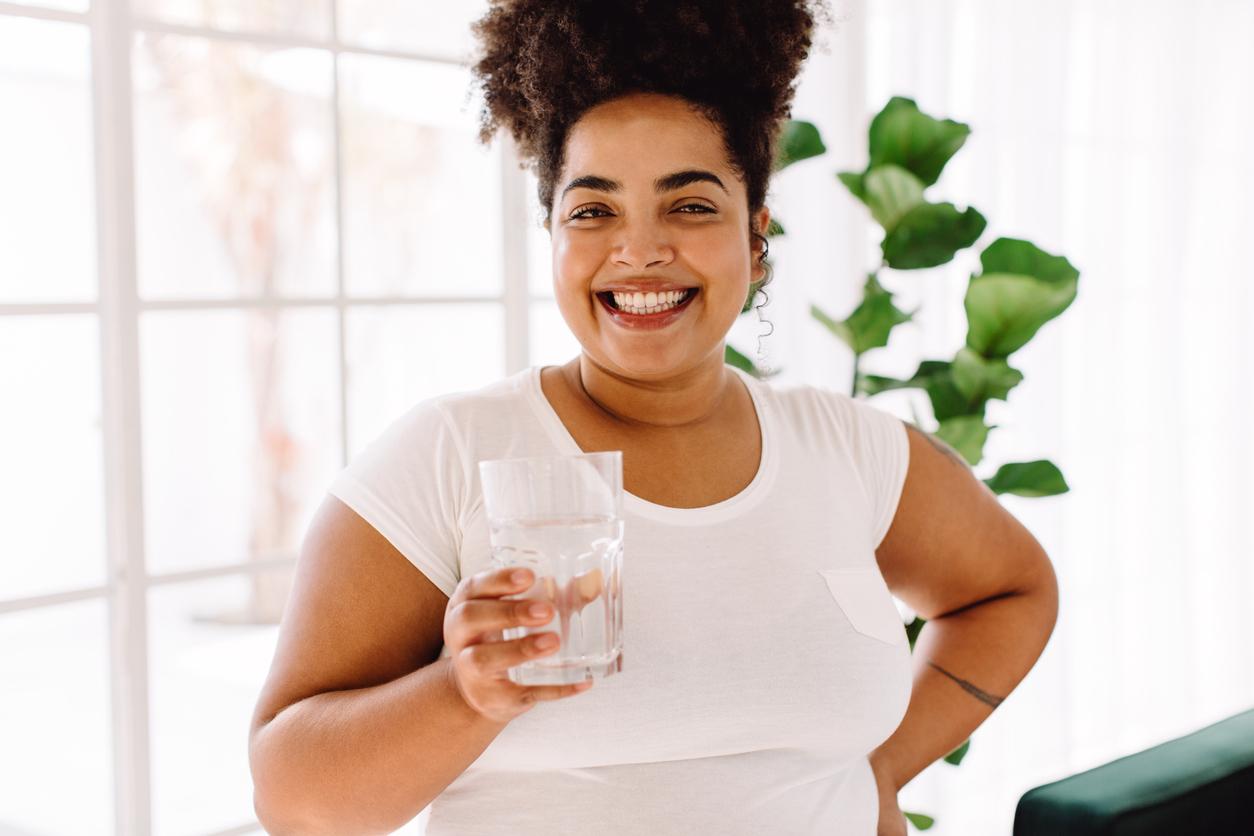Beautiful woman stands in her kitchen and smiles while holding a glass of water