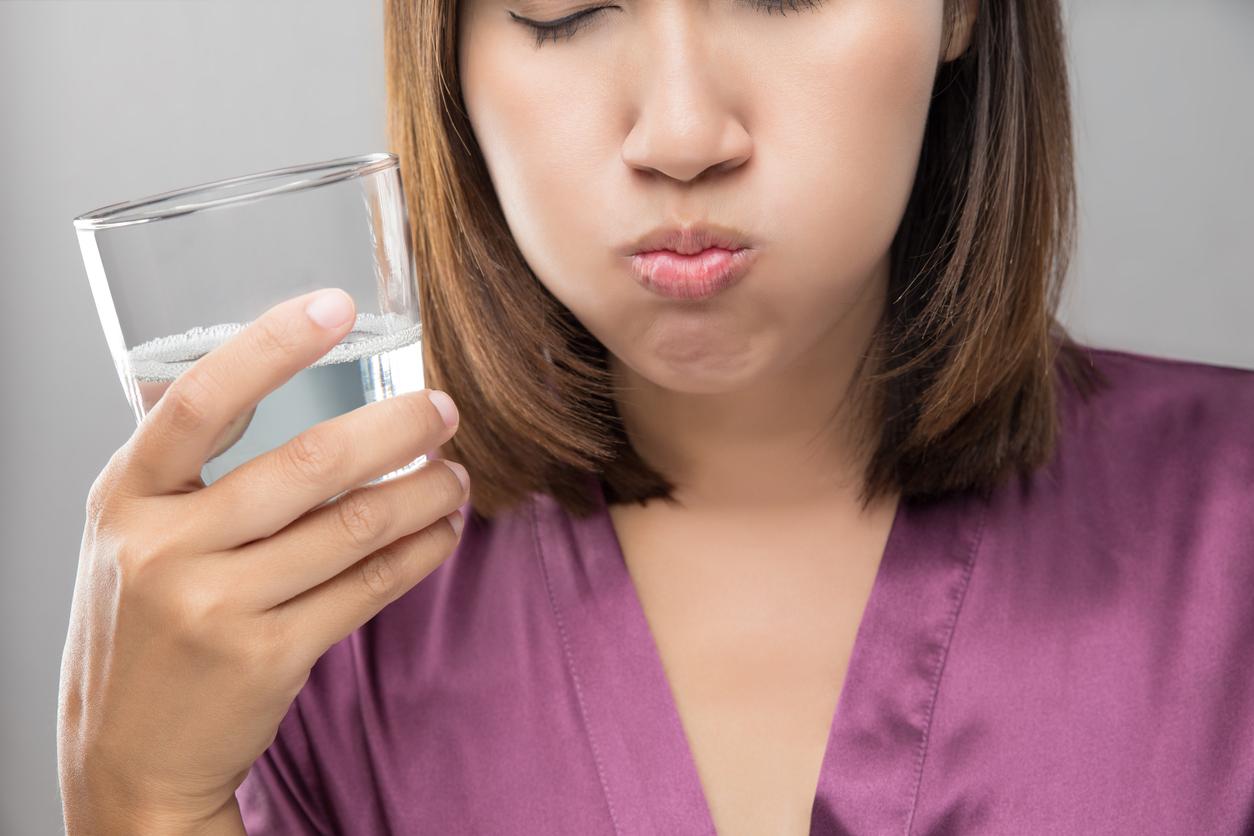 Attractive woman wearing a pretty plum colored shirt holds a glass of clear liquid and rinses her mouth