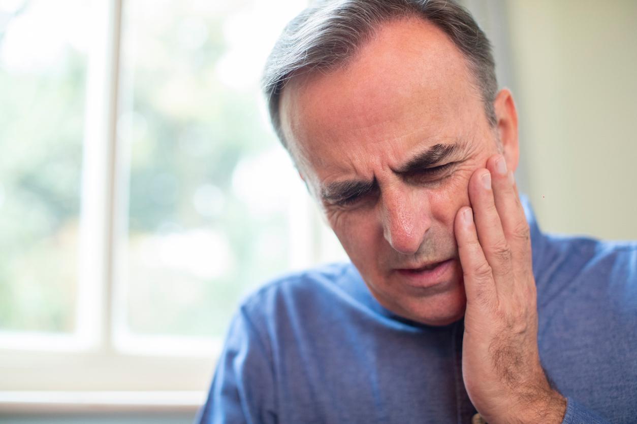 Mature white main with graying hair grimaces in pain as he touches his jaw